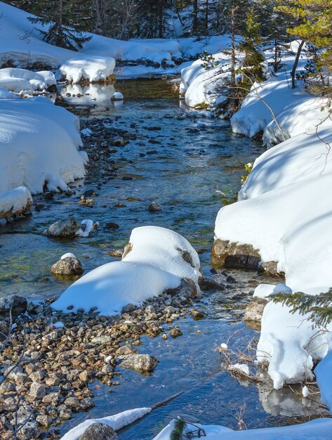 Foto córrego da pequena montanha com monte de neve nas pedras.