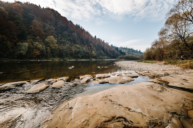 Córrego do rio de fluxo rápido da montanha de água nas rochas com céu azul.