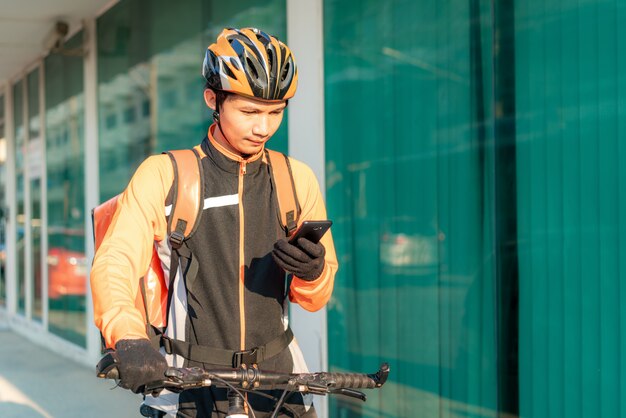 Correio asiático do homem que verifica o endereço do cliente no mapa no smartphone na bicicleta que entrega alimentos