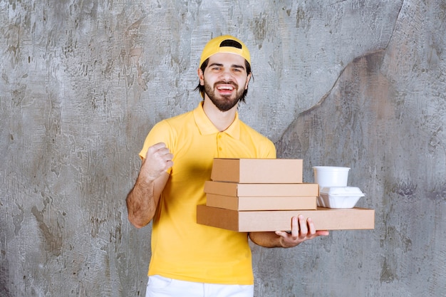 Correio com uniforme amarelo segurando pacotes para viagem e caixas de papelão e mostrando sinal positivo