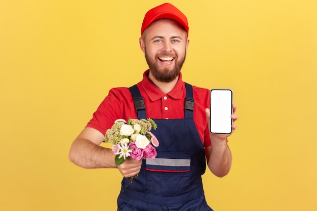 Correio de homem em pé com flores nas mãos mostrando celular com tela vazia para propaganda