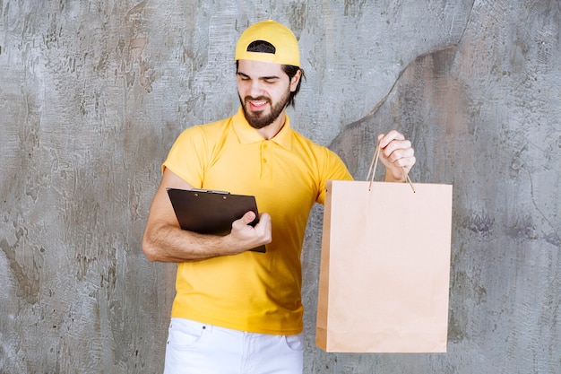 Correio de uniforme amarelo segurando uma sacola de compras de papelão e lendo a pasta de endereços