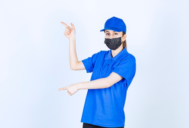 Correio feminino com máscara e uniforme azul apontando para o lado esquerdo.