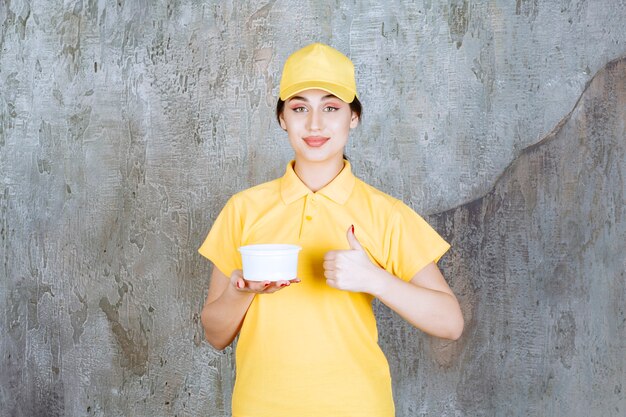 Correio feminino em uniforme amarelo, segurando uma xícara para viagem e apreciando o produto.