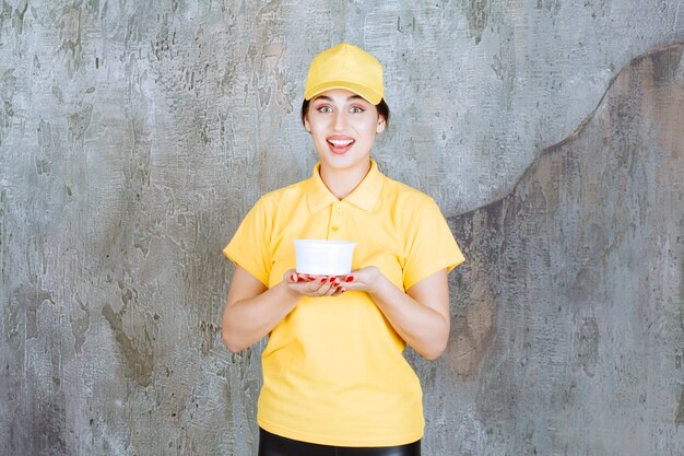 Correio feminino em uniforme amarelo, segurando uma xícara para viagem.