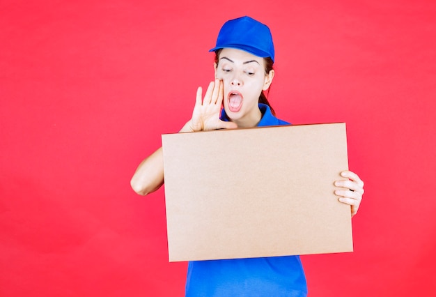 Correio feminino em uniforme azul segurando uma caixa de pizza de papelão para viagem e se divertindo.
