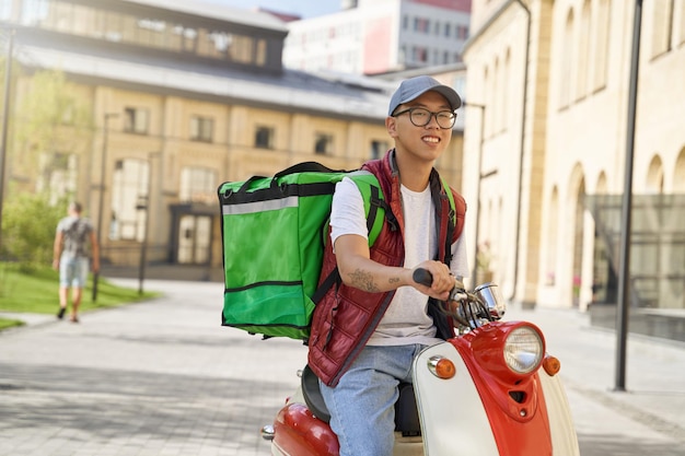 Correio masculino asiático alegre jovem com saco térmico montando motor s