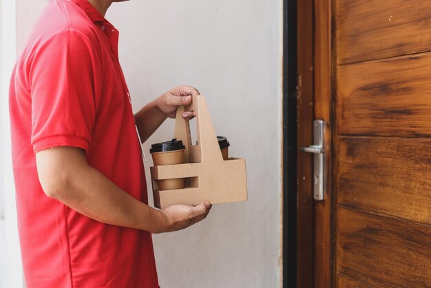 correio masculino em uniforme vermelho entregando xícaras de café ao cliente na frente da casa