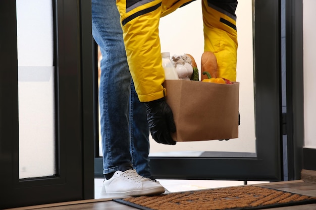 Correio traz sacola de papel com comida para porta fechada Serviço de entrega durante a quarentena devido ao surto de Covid19