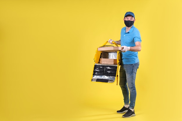 Foto correio usando máscara de proteção contra vírus e luvas de entrega de alimentos medicinais com saco térmico aberto amarelo