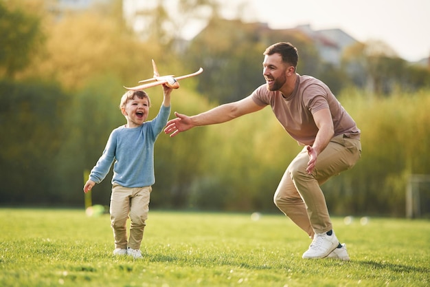 Correndo com um avião de brinquedo Um pai feliz com o filho estão se divertindo no campo no verão