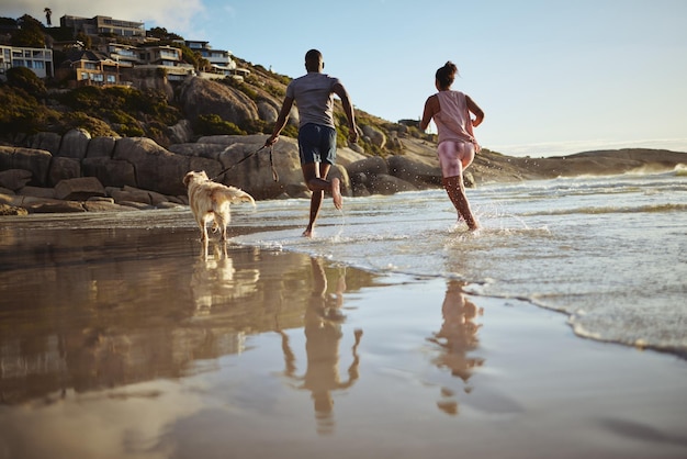 Correndo fitness e cachorro com casal na praia e treinando para exercícios de saúde e exercícios juntos Amor liberdade e bem-estar com homem e mulher corredor com animal de estimação à beira-mar para esportes e verão