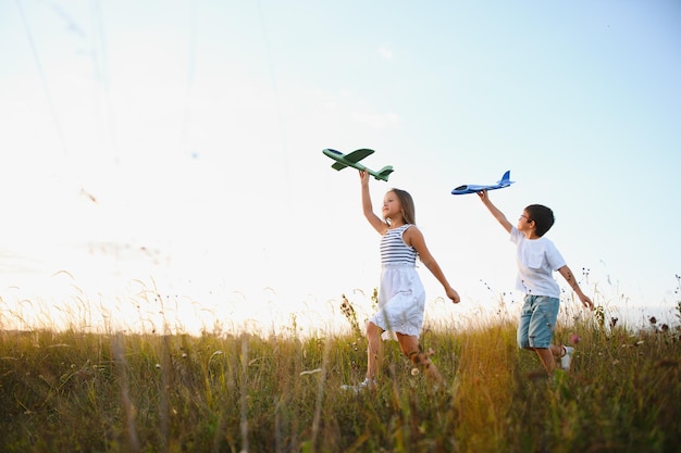 Correndo menino e menina segurando dois aviões verdes e azuis brinquedo no campo durante o dia ensolarado de verão