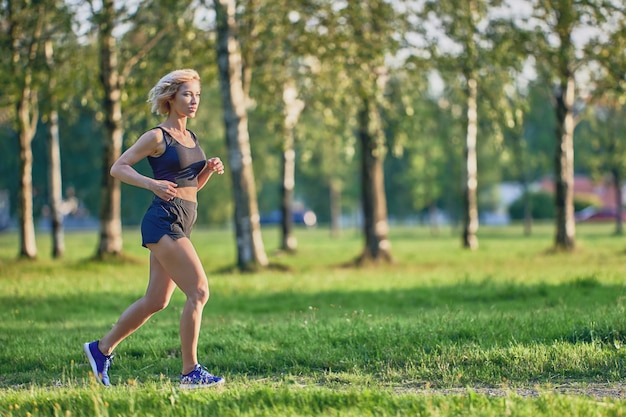 Correndo no parque por uma mulher esguia em roupas esportivas no dia de verão