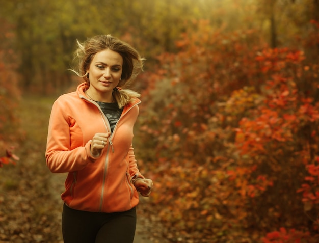 Correndo pela floresta de outono. uma jovem apta em roupas esportivas corre ao longo de um caminho na floresta com folhas avermelhadas. conceito de estilo de vida saudável