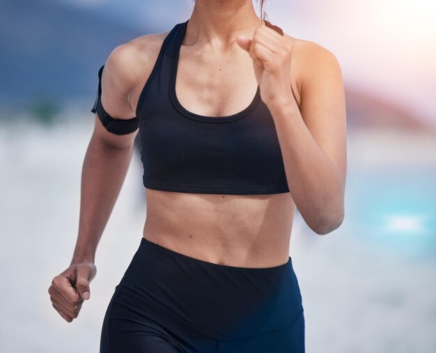 Correr cuerpo y mujer en una playa para entrenamiento físico y salud de rendimiento y entrenamiento en un fondo borroso Bienestar deportivo y corredora en el mar para desafío de resiliencia o carrera oceánica