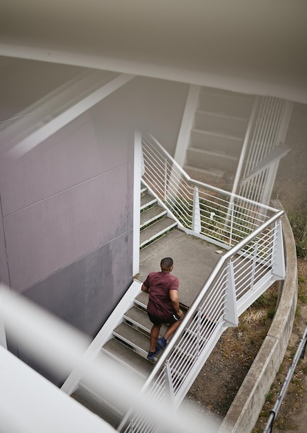 Correr fitness y vista superior del hombre negro en las escaleras para el bienestar de la salud y el ejercicio Entrenamiento deportivo y ejercicio de trote de corredor masculino o entrenamiento cardiovascular en pasos al aire libre para la fuerza y la resistencia