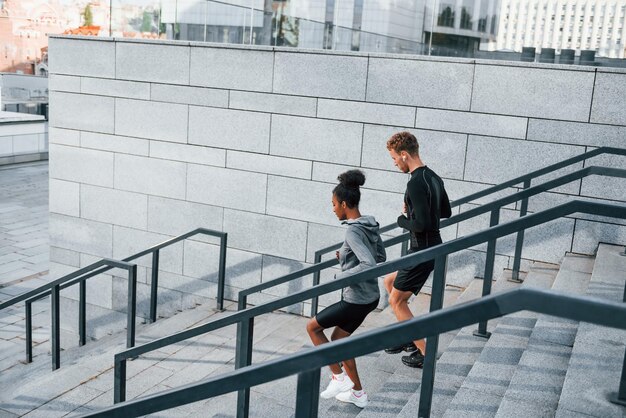 Correr en gradas Un hombre europeo y una mujer afroamericana con ropa deportiva hacen ejercicio juntos