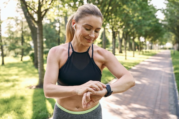 Correr por la mañana hermosa mujer deportiva en ropa deportiva y auriculares mirando su reloj comprobando el