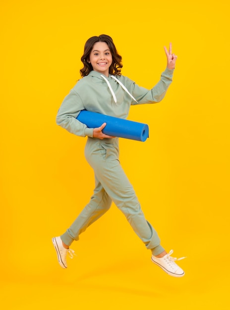 Correr y saltar Longitud total de una jovencita fitness en ropa deportiva con colchoneta de yoga posando sobre amarillo