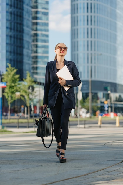 Corretor de imóveis feminino em um blazer está passeando com um laptop no distrito financeiro