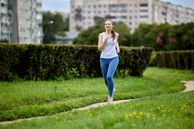 Corrida matinal em parque público perto da área residencial da cidade na primavera por uma mulher esbelta em roupas esportivas