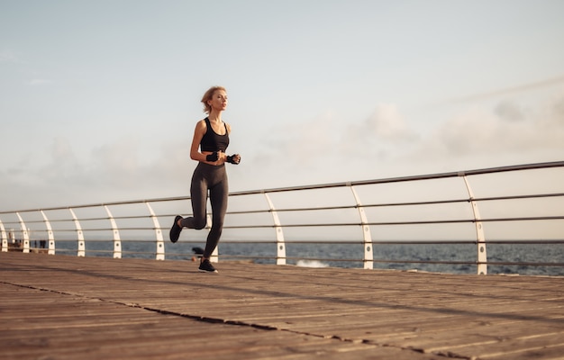 Corrida matinal. Jovem mulher atlética em roupas esportivas corre na praia ao nascer do sol