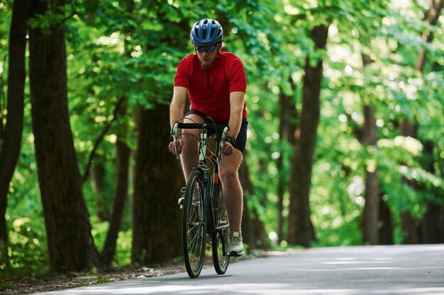 Corriendo hacia adelante. Ciclista en bicicleta está en la carretera asfaltada en el bosque en día soleado