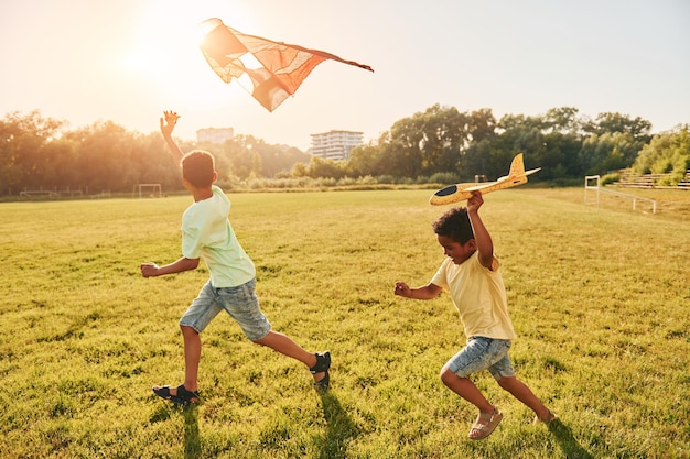 Corriendo con cometa Dos niños afroamericanos se divierten juntos en el campo durante el día de verano