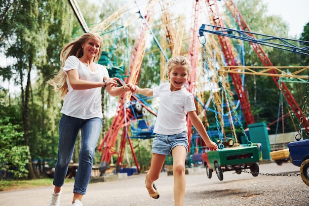 Corriendo y jugando. Niña alegre que su madre pasa un buen rato en el parque junto a las atracciones.