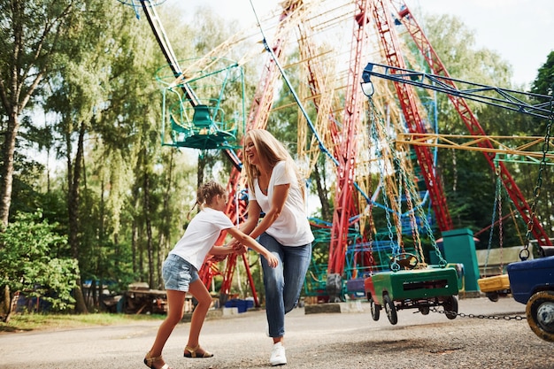 Corriendo y jugando. Niña alegre que su madre pasa un buen rato en el parque junto a las atracciones.