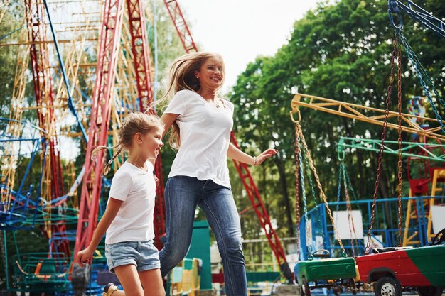 Corriendo y jugando. Niña alegre que su madre pasa un buen rato en el parque junto a las atracciones.