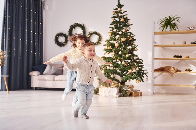 Corriendo juntos El hermano y la hermana pequeños están en la habitación decorada con Navidad