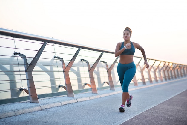 Corriendo muy rápido. Mujer con sobrepeso de piel oscura con zapatillas cómodas corriendo muy rápido