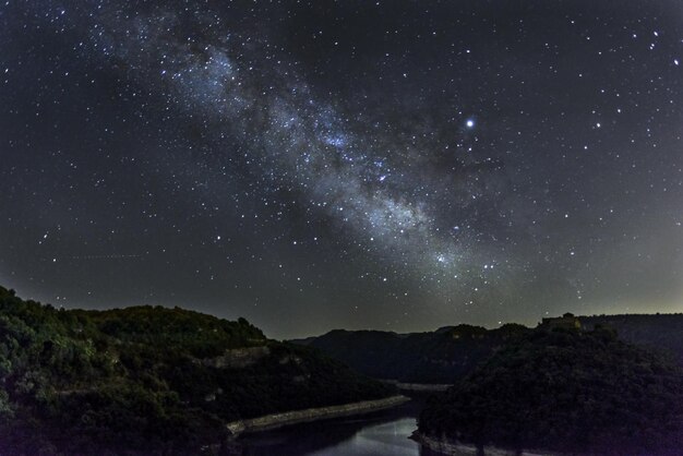 Corriente de agua rodeada de colinas bajo el cielo estrellado de la noche