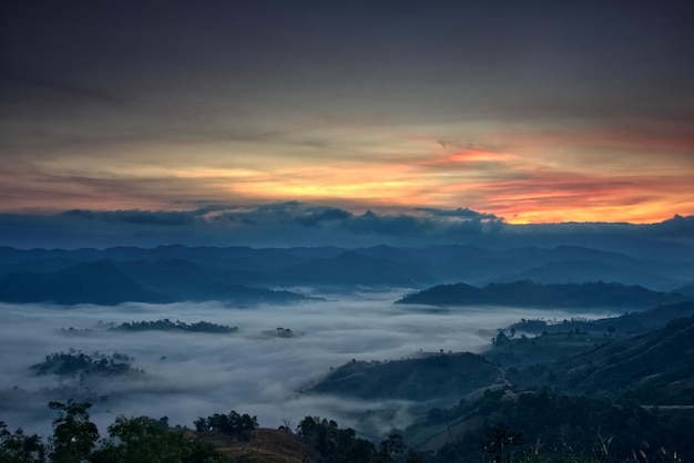 La corriente de niebla esponjosa cubre un valle con un colorido cielo crepuscular en una mañana