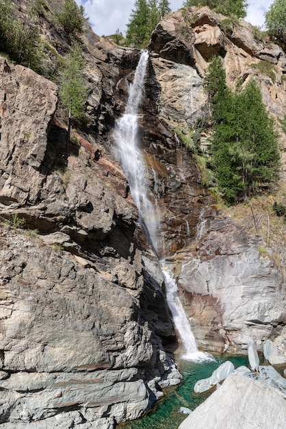 Las corrientes de agua sobre rápidos de granito en el lago esmeralda rodeado de árboles vertical Valle de Aosta