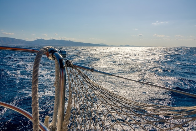 Corrimão de iate e costa no horizonte. Caminho solar na água com ondas