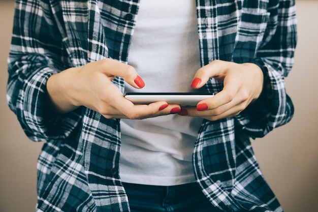 Foto cortada a imagem da mulher de camisa xadrez com manicure vermelho tem telefone inteligente nas mãos