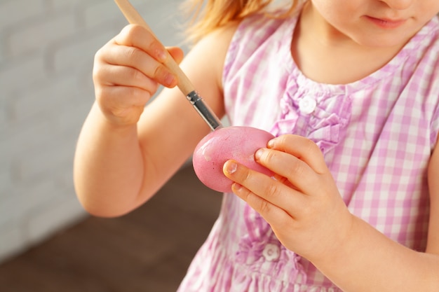 Cortada a imagem de uma menina pintando ovos para a Páscoa