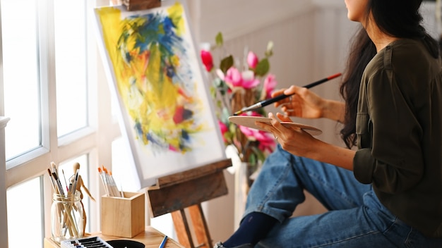 Cortada a imagem do jovem artista linda segurando um pincel e desenhando na tela de pintura