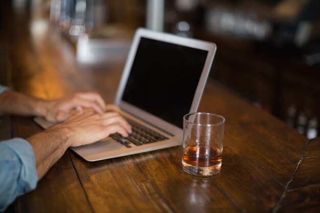 Cortadas as mãos usando o laptop pelo copo de cerveja no pub