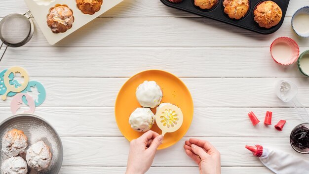 Cortado de mulher decorando cupcakes com estêncil na mesa com ferramentas de cozimento