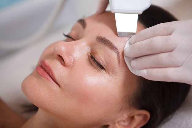 Cortado em close de uma bela mulher madura recebendo tratamento facial ultrassônico pela esteticista