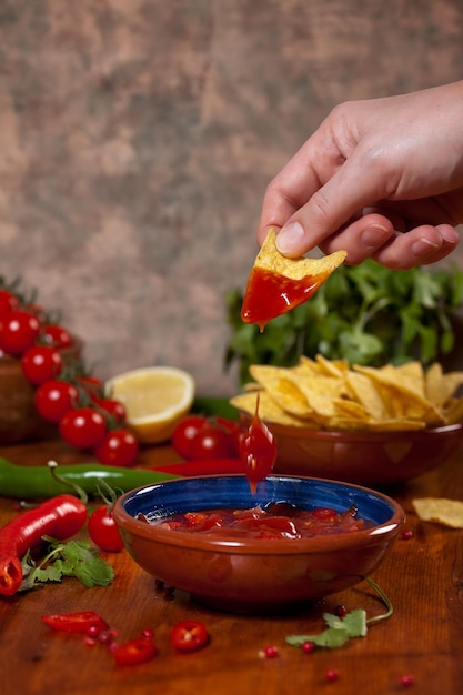 Foto cortado a mano sumergiendo nachos en salsa en la mesa