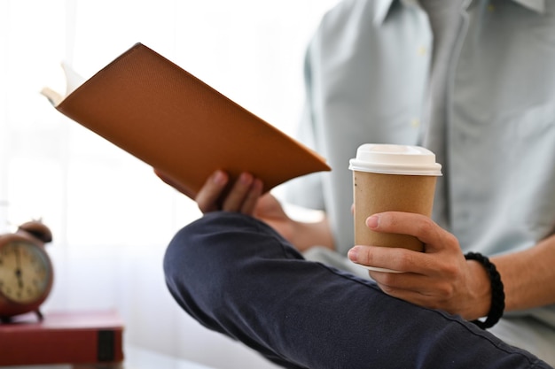 Cortado um homem asiático casual lendo um livro enquanto toma café na cafeteria