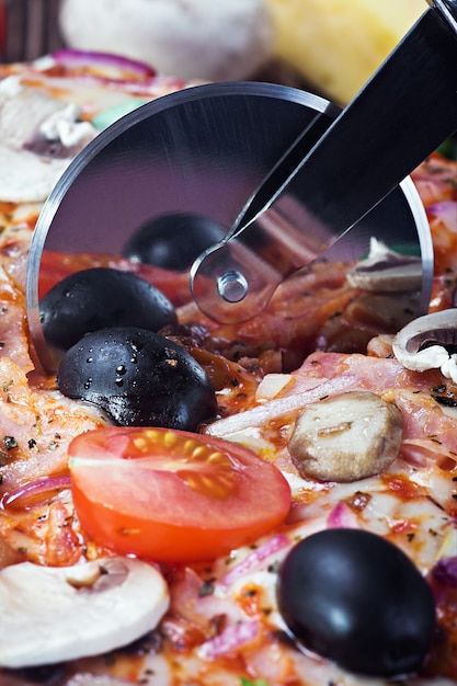 Cortador corta una pizza fresca con champiñones