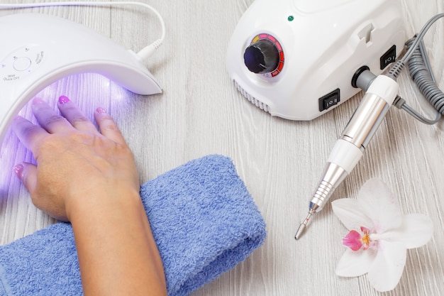 Cortador de fresagem e lâmpada ultravioleta led com mão de mulher em fundo cinza de madeira. Um conjunto de ferramentas cosméticas para manicure profissional de hardware. Vista do topo