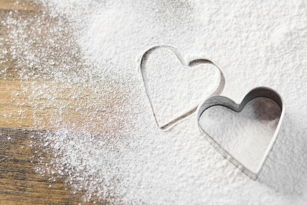 Cortador de galletas en forma de corazón sobre la mesa de la cocina y harina