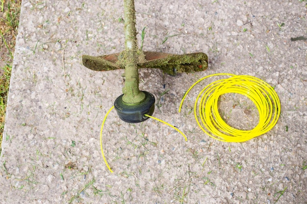 Una cortadora de césped con hilo de pescar después de cortar el césped y un rollo de hilo de pescar nuevo cerca Reemplazo de consumibles en la recortadora